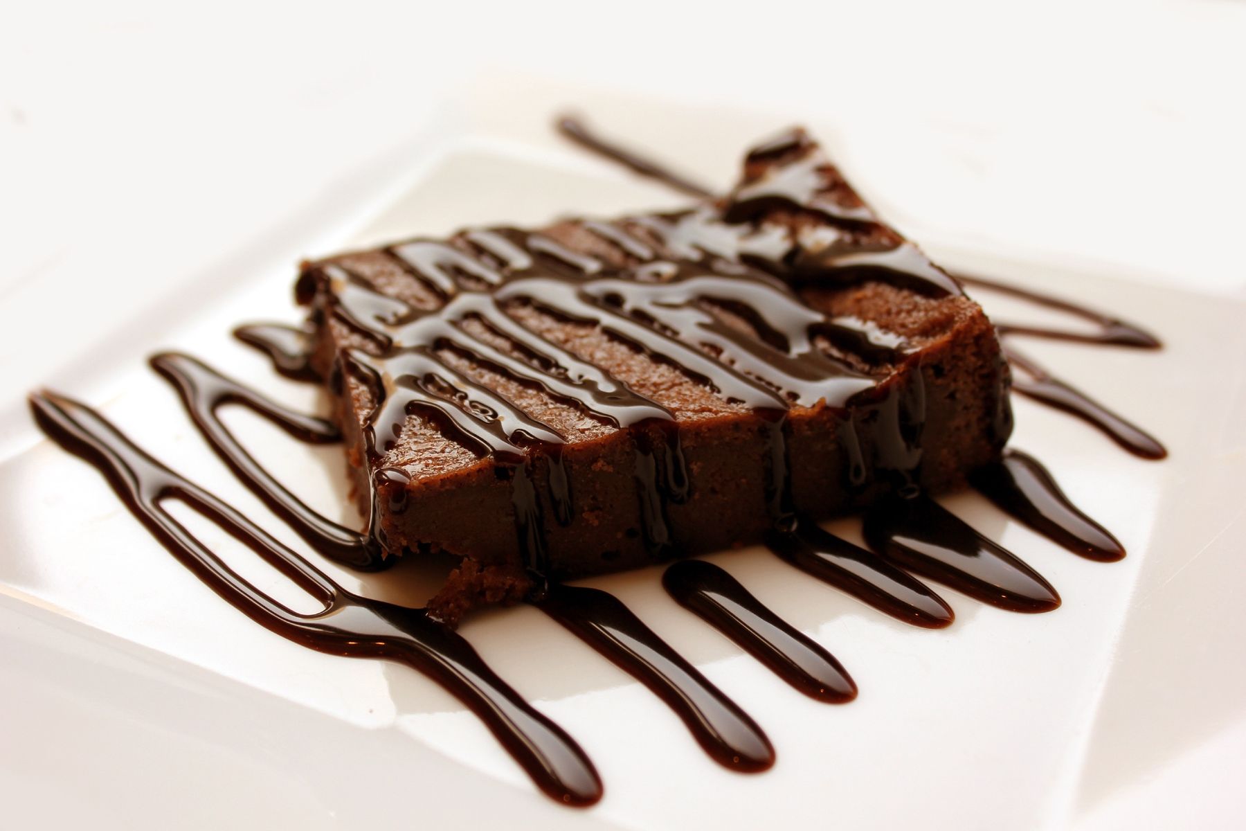 En bit chokladbrownie med chokladdrizzle på en vit tallrik.