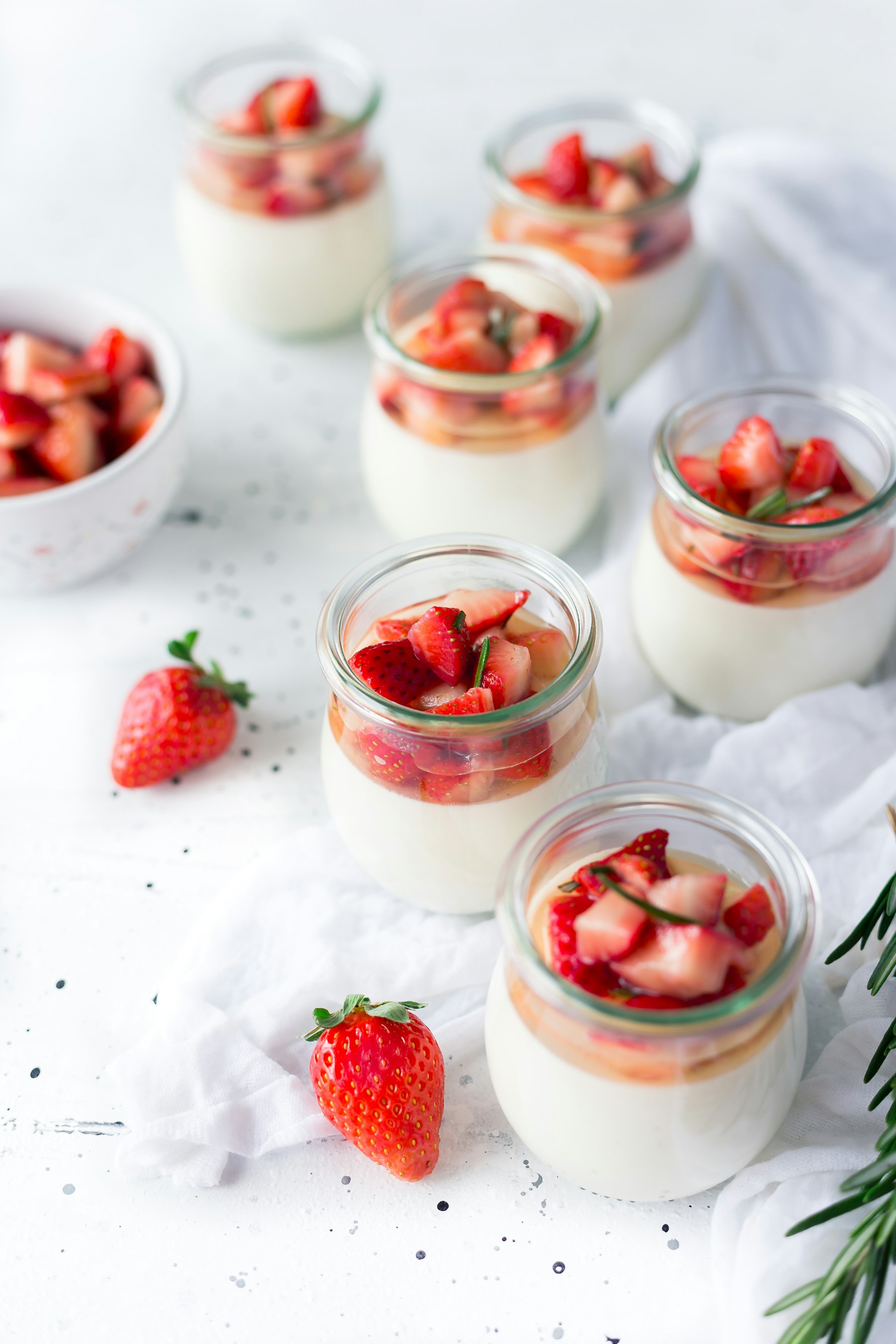 Fyra små glasburkar med ljus pudding och hackade jordgubbar på toppen.