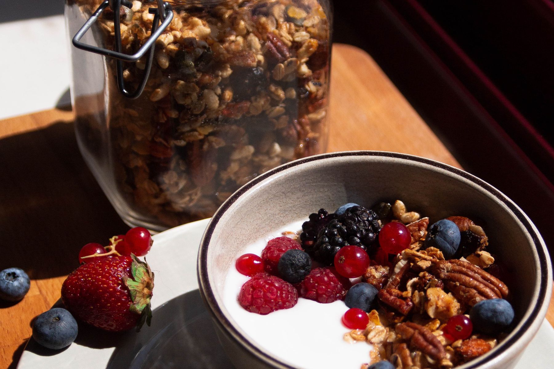 Skål med yoghurt, färska bär och granola på träbord.