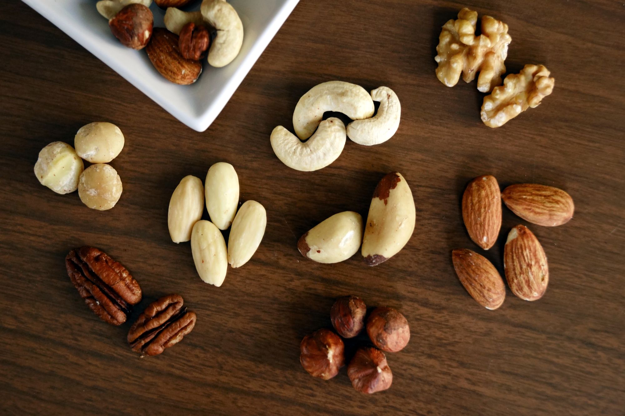 Mandel, cashew, valnötter och hasselnötter utspridda på ett mörkt träbord.