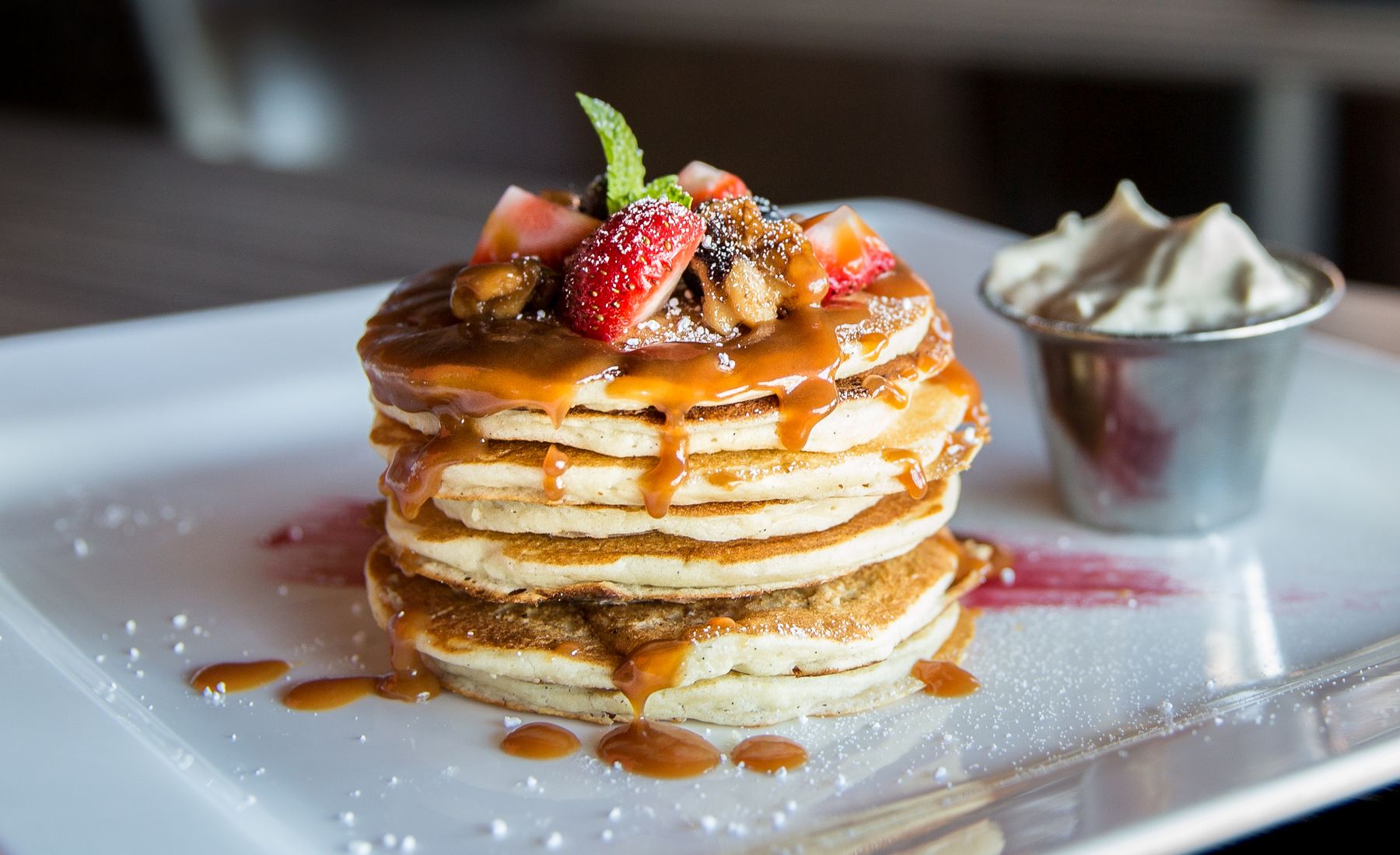 En stapel pannkakor med bär på en vit tallrik.